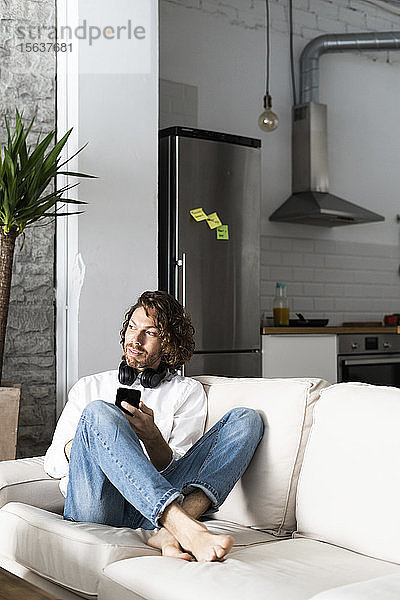 Entspannter Mann sitzt zu Hause auf Couch mit Handy