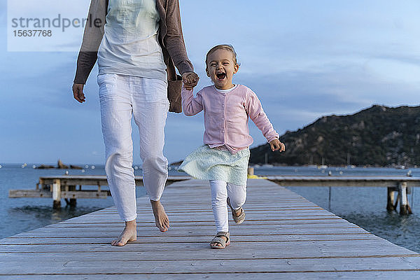 Glückliches Mädchen geht mit der Mutter bei Sonnenuntergang auf einem Steg spazieren