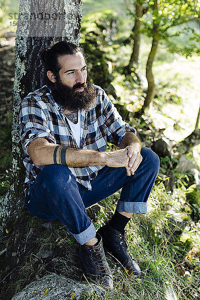 Mann mit Bart sitzt am Baumstamm im Wald