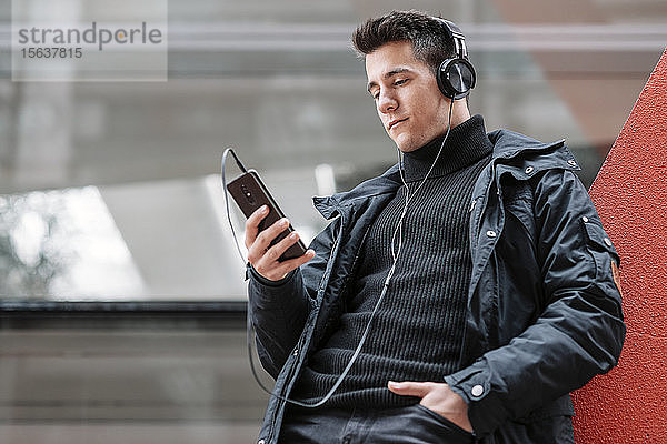 Junger Mann mit Smartphone und Kopfhörern beim Musikhören