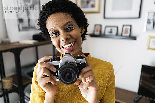 Porträt einer lächelnden jungen Frau mit Oldtimer-Kamera zu Hause