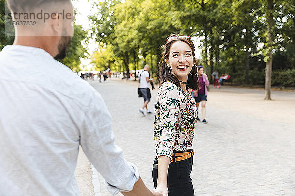 Porträt einer glücklichen jungen Frau  die Hand in Hand mit ihrem Freund in einem Park geht