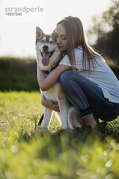 Junge Frau umarmt ihren Hund auf einer Wiese