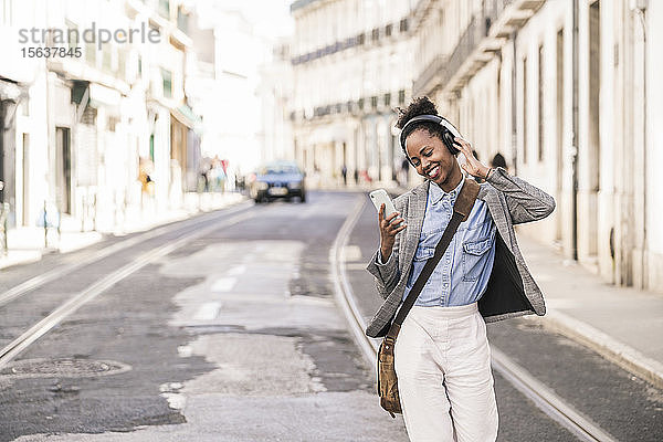 Glückliche junge Frau mit Kopfhörern und Mobiltelefon in der Stadt unterwegs  Lissabon  Portugal