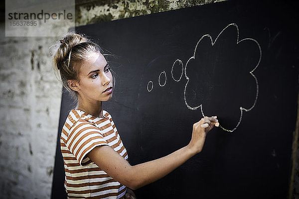 Nachdenkliche junge Frau  die eine Gedankenblase auf eine Tafel zeichnet
