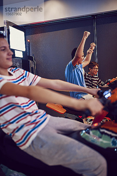 Teenager-Freunde spielen und vergnügen sich mit einem Fahrsimulator in einer Spielhalle
