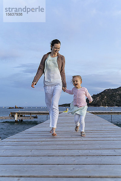 Glückliche Mutter mit Tochter geht bei Sonnenuntergang auf einem Steg spazieren