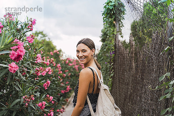 Porträt einer lächelnden jungen Frau mit Rucksack beim Spaziergang in einem Park