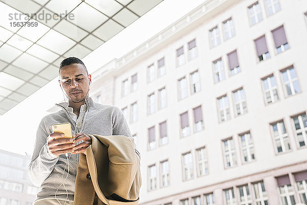 Porträt eines Geschäftsmannes mit Kopfhörern mit Smartphone in der Stadt