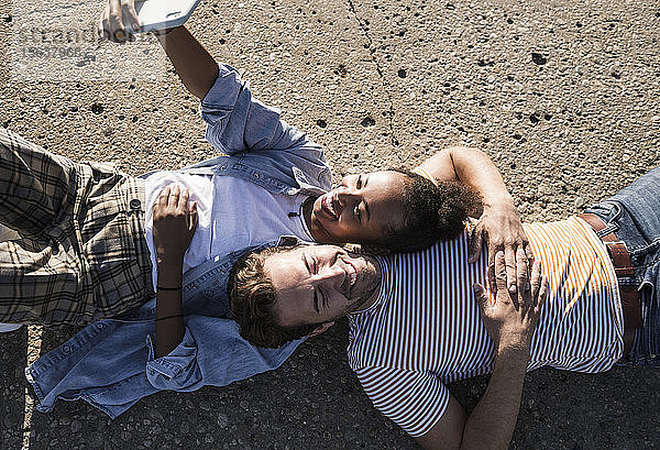 Glückliches junges Paar liegt auf dem Betonboden und macht sich ein Selfie