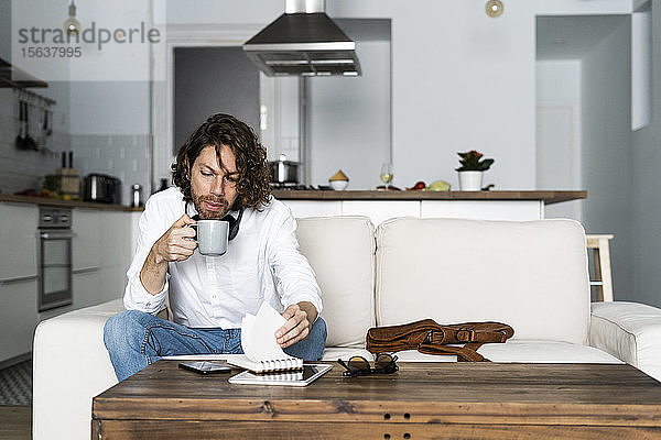 Mann sitzt zu Hause auf dem Sofa mit Kaffeetasse und Notizblock