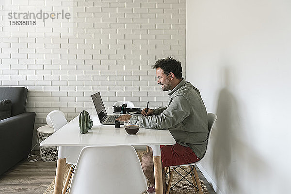 Mann sitzt am Tisch und arbeitet an Grafiktablett und Laptop