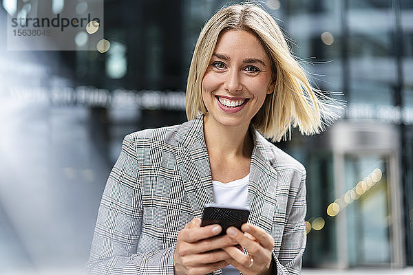 Porträt einer glücklichen jungen Geschäftsfrau mit Mobiltelefon in der Stadt