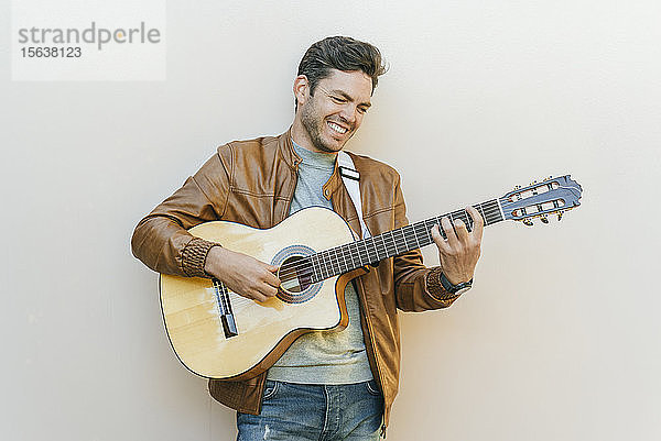Lächelnder Mann spielt Gitarre vor einer Wand