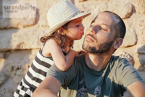 Kleines Mädchen küsst ihren Vater bei Sonnenuntergang