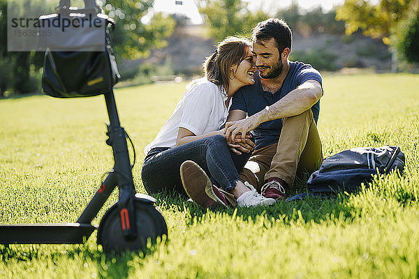 Glückliches Paar mit Elektroroller entspannt sich auf einer Wiese in einem Park