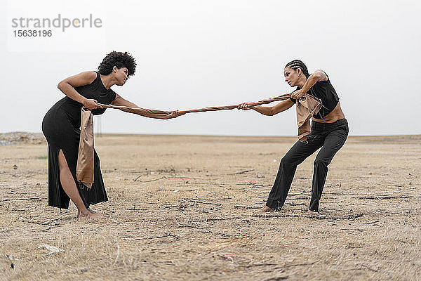 Zwei Frauen ziehen ein Tuch in trostloser Landschaft