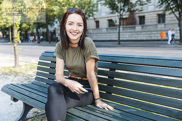 Porträt einer lächelnden jungen Frau  die mit einem Smartphone auf einer Bank sitzt