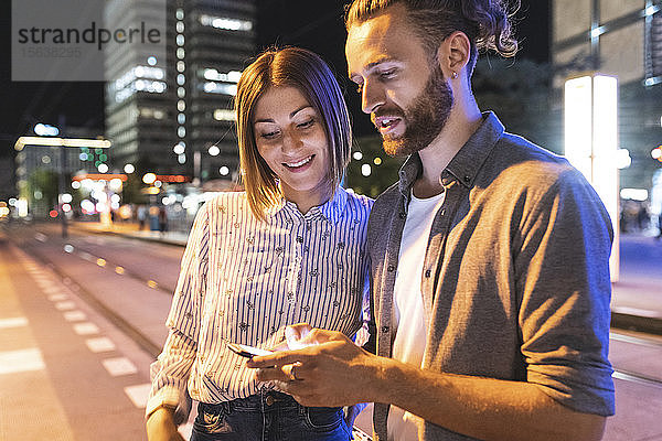 Glückliches Paar in der Stadt  das nachts sein Telefon kontrolliert  Berlin  Deutschland