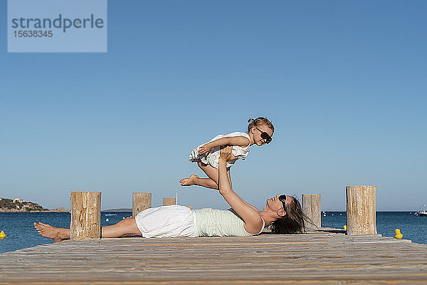Glückliche Mutter hebt ihre Tochter auf einem Steg am Meer hoch