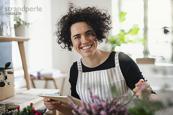 Porträt einer glücklichen jungen Frau mit Klemmbrett in einem kleinen Laden mit Pflanzen