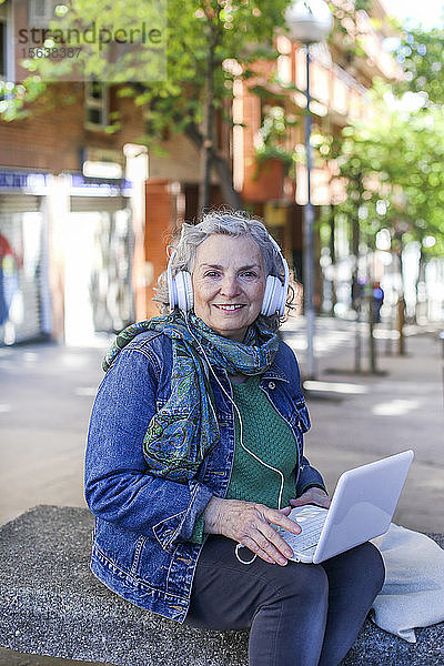 Porträt einer älteren Frau mit Kopfhörern und Laptop in der Stadt