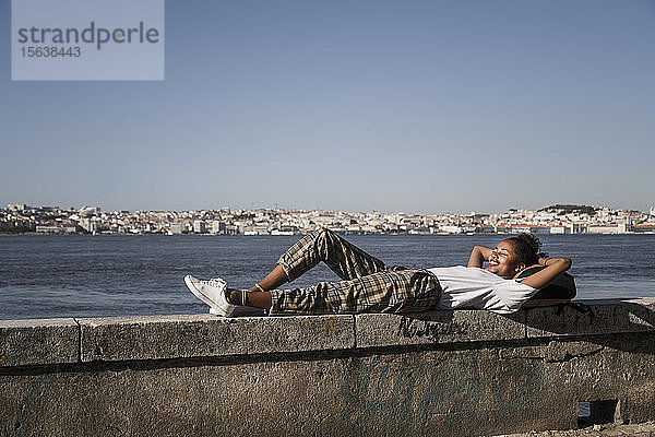 Junge Frau auf einer Mauer am Wasser liegend  Lissabon  Portugal