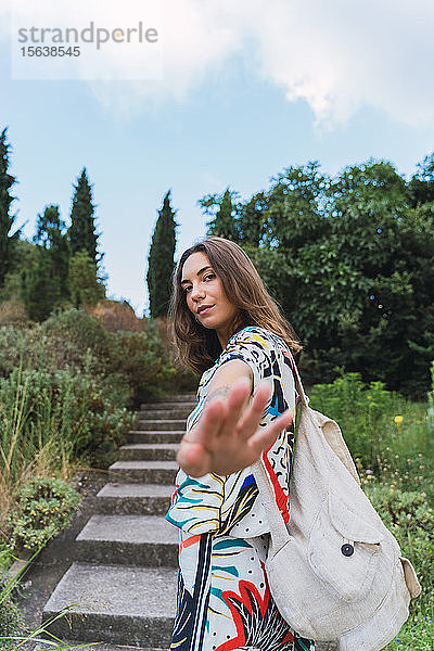 Porträt einer jungen Frau mit Rucksack in einem Park  die die Hand hebt