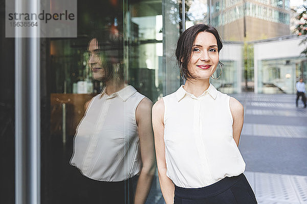 Porträt einer selbstbewussten jungen Geschäftsfrau im Spiegel der Glasfront  Berlin  Deutschland