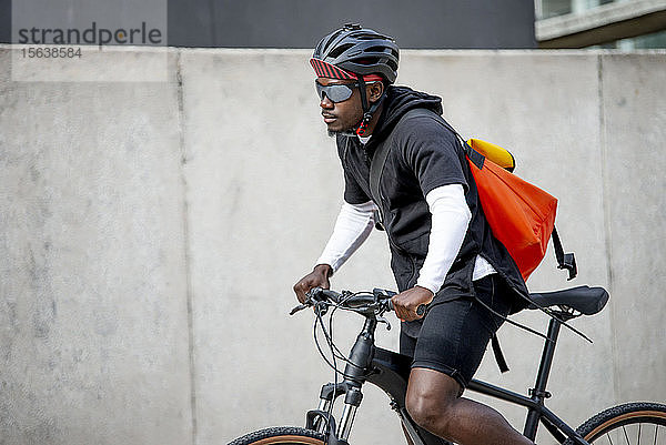 Stilvoller junger Mann mit Kuriertasche beim Fahrradfahren in der Stadt
