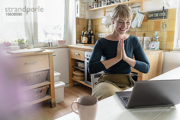 Porträt einer lachenden Frau mit Laptop  die in der Küche Yoga praktiziert