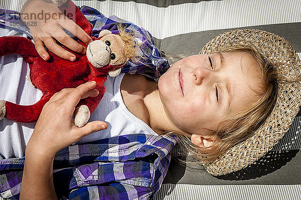 Kleines Mädchen mit Kuscheltier im Sonnenschein liegend