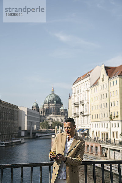 Porträt eines Geschäftsmannes  der auf einer Brücke steht und auf ein Smartphone schaut  Berlin  Deutschland