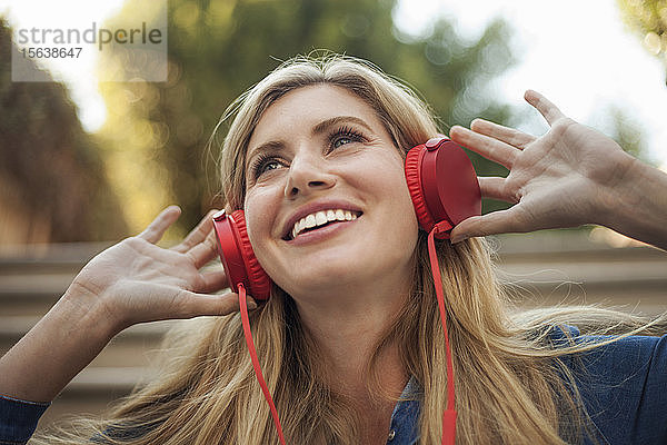 Porträt einer lächelnden Frau  die mit roten Kopfhörern Musik hört