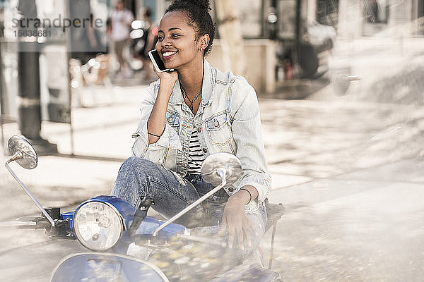 Glückliche junge Frau mit Motorroller am Telefon in der Stadt  Lissabon  Portugal