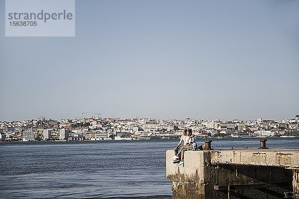 Junges Paar sitzt am Pier am Wasser  Lissabon  Portugal
