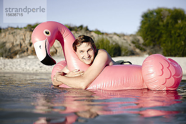 Junger Mann mit Flamingo-Pool schwimmt im See