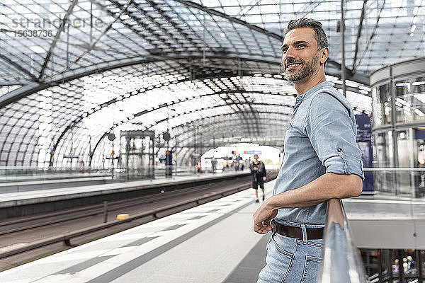Lächelnder Mann am Bahnhof beim Warten auf den Zug