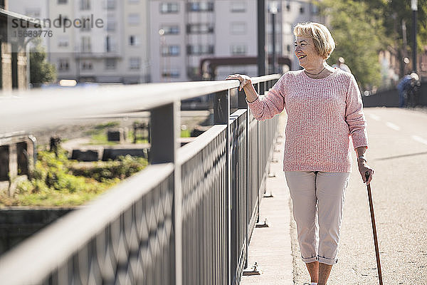 Ältere Frau  die auf einer Fußgängerbrücke geht  Gehstock benutzt und wegschaut