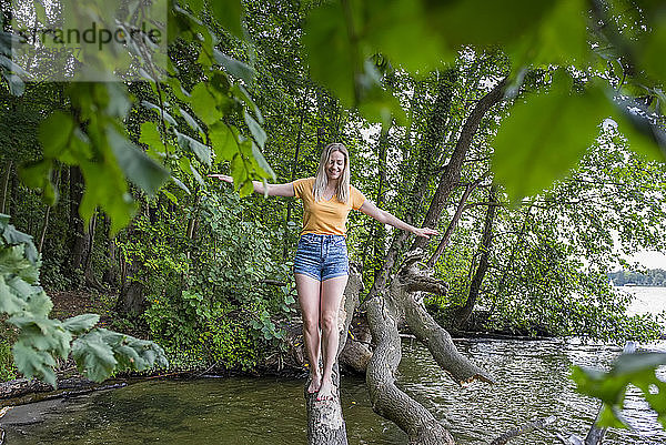 Lächelnde Frau balanciert auf einem Baumstamm am Seeufer