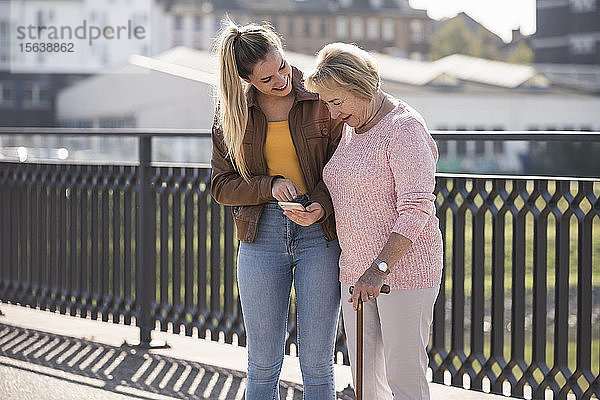 Enkelin und ihre Großmutter gehen auf einem Steg und benutzen ein Smartphone