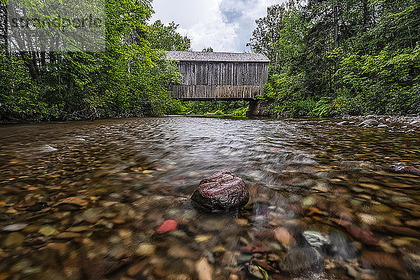Historische überdachte Brücke über einen flachen Bach und Fokus auf einen kleinen Felsen; Saint John  New Brunswick  Kanada
