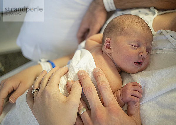Neugeborenes Baby schläft auf der Brust der Mutter in einem Krankenhausbett  die Hände von Mutter und Vater sind sichtbar; Vancouver  British Columbia  Kanada