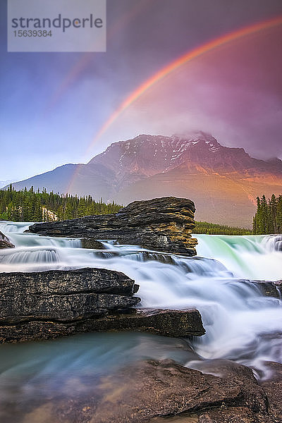 Ein doppelter Regenbogen leuchtet über einem schroffen Wasserfall und den Rocky Mountains  Jasper National Park; Alberta  Kanada