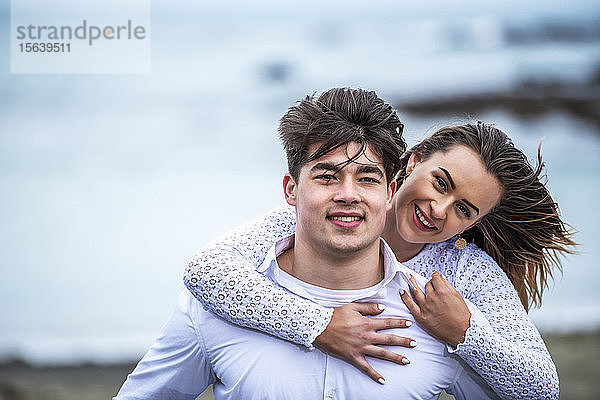 Porträt eines jungen Paares mit vom Wind zerzausten Haaren am Strand; Wellington  Nordinsel  Neuseeland