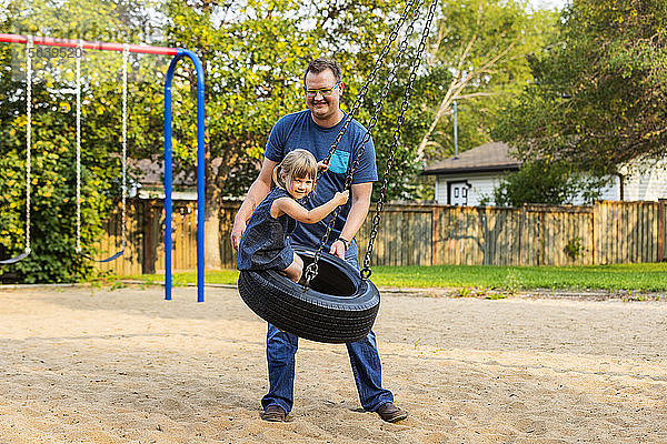 Ein Vater schiebt seine Tochter auf einer Reifenschaukel auf einem Spielplatz; Edmonton  Alberta  Kanada