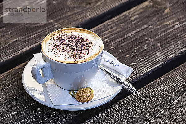 Cappuccino in einem italienischen Cafe auf einem Holztisch  serviert mit einem kleinen Keks; Hexham  Northumberland  England