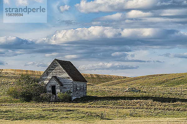 Alte  verlassene  von den Jahren in der Prärie verwitterte Landkirche und ein Oldtimer auf dem Feld dahinter; Val Marie  Saskatchewan  Kanada