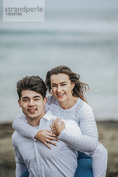 Porträt eines jungen Paares am Strand  die junge Frau wird auf dem Rücken des jungen Mannes getragen; Wellington  Nordinsel  Neuseeland