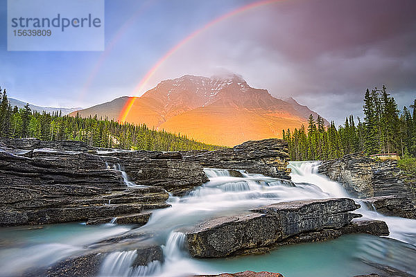 Ein doppelter Regenbogen leuchtet über einem schroffen Wasserfall und den Rocky Mountains  Jasper National Park; Alberta  Kanada